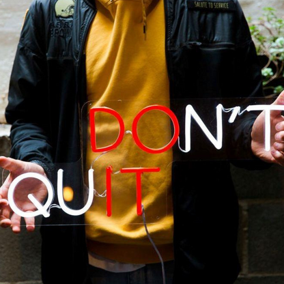 a person holding don't quit neon sign